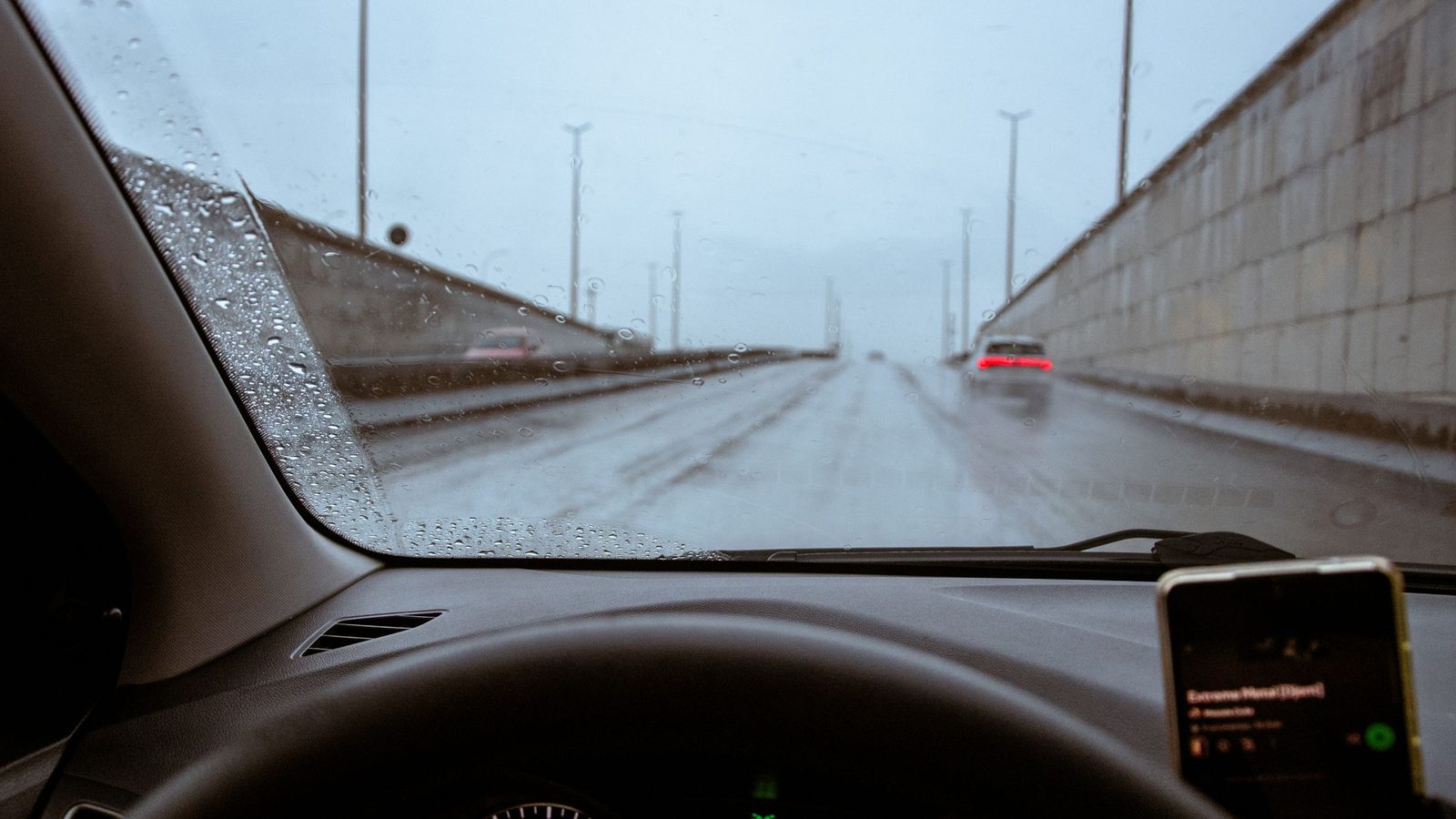 Vista do interior de um carro em uma via de Brasilia em dia de chuva, com o para-brisa molhado.
