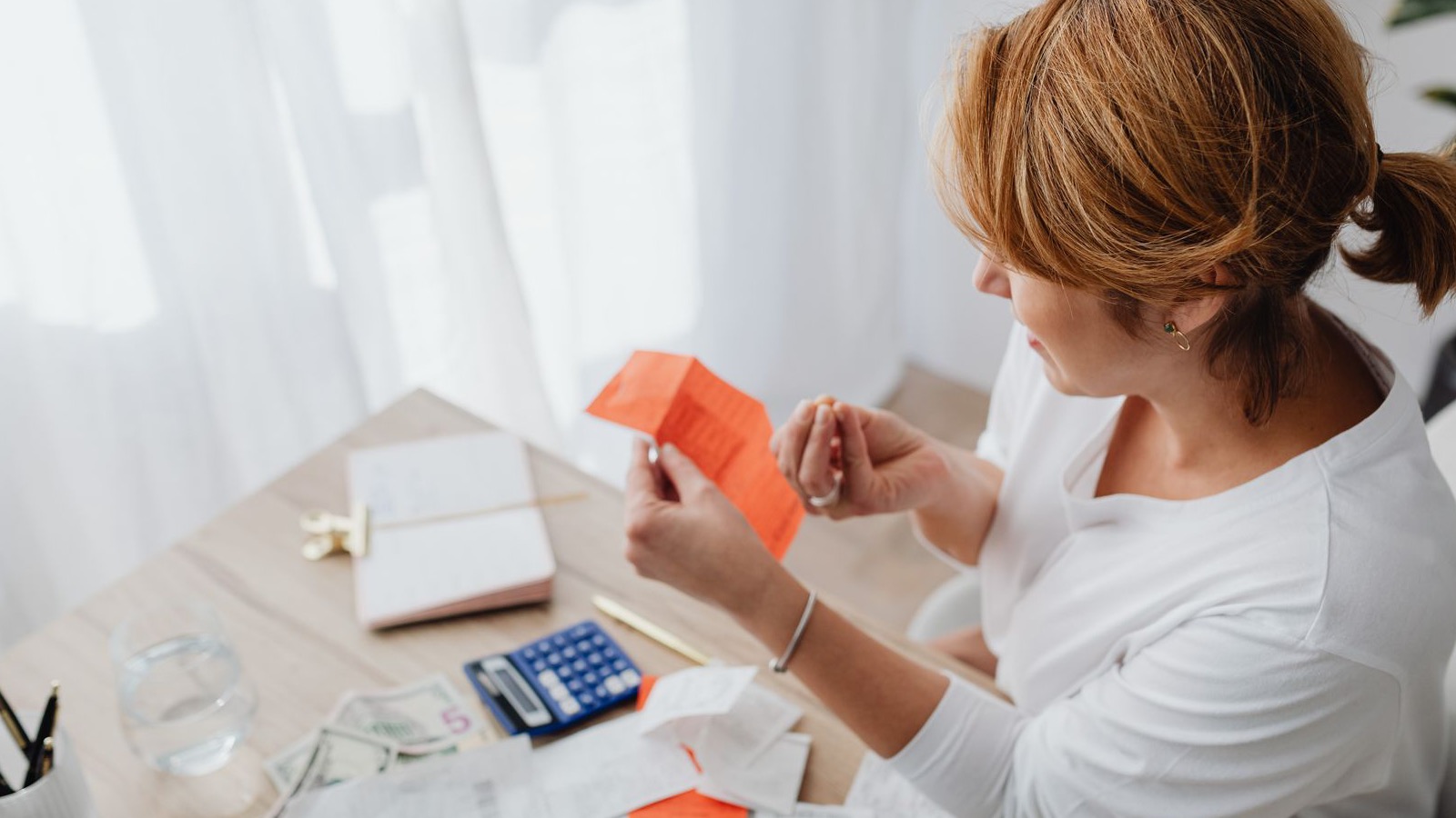 Pessoa organizando contas, recibos e calculadora sobre a mesa para colocar os serviços da casa no próprio nome.