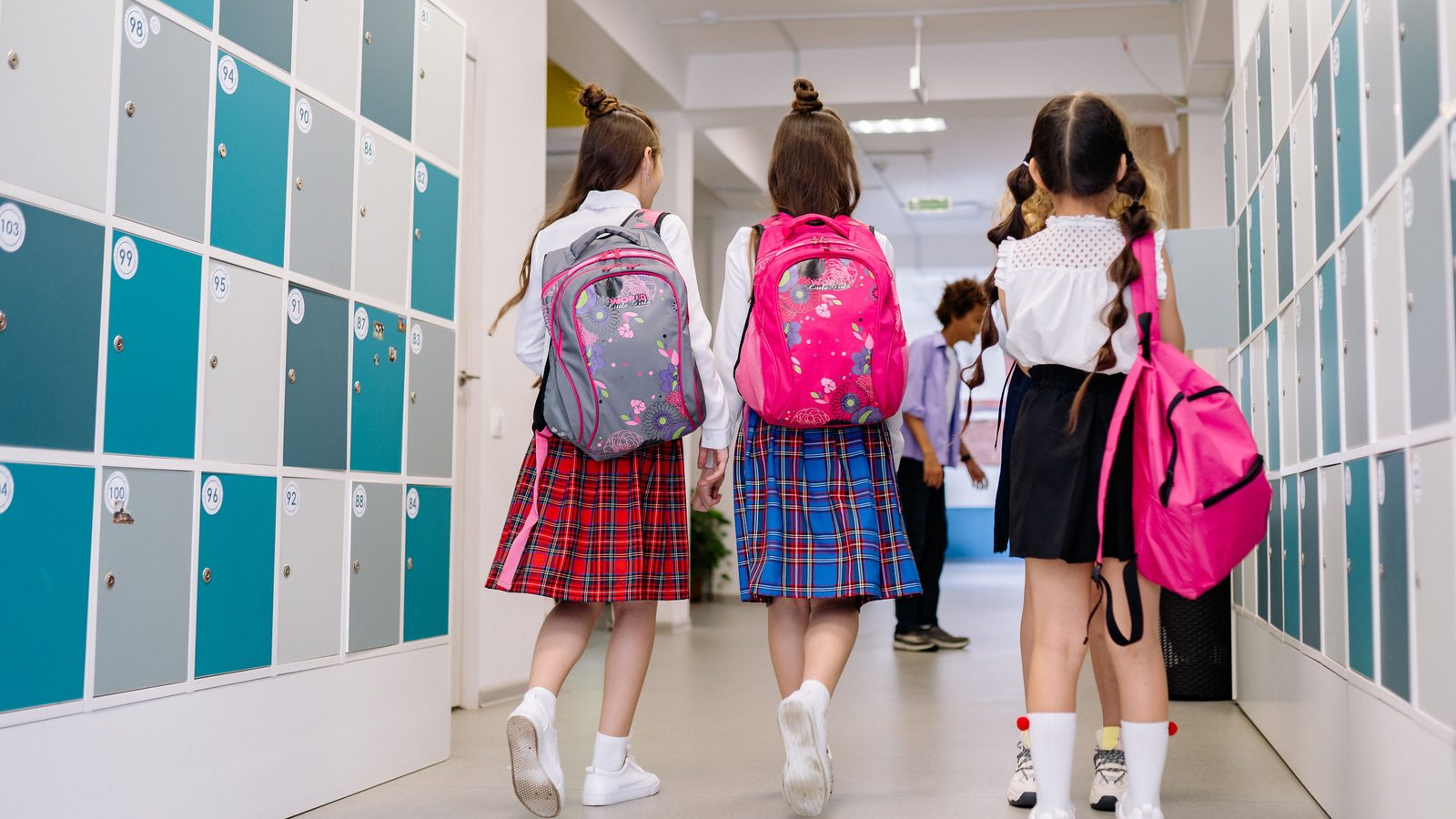 Estudantes com mochilas caminhando pelo corredor da escola no início do turno.