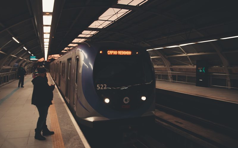 Trem chegando à estação com passageiros esperando na plataforma.