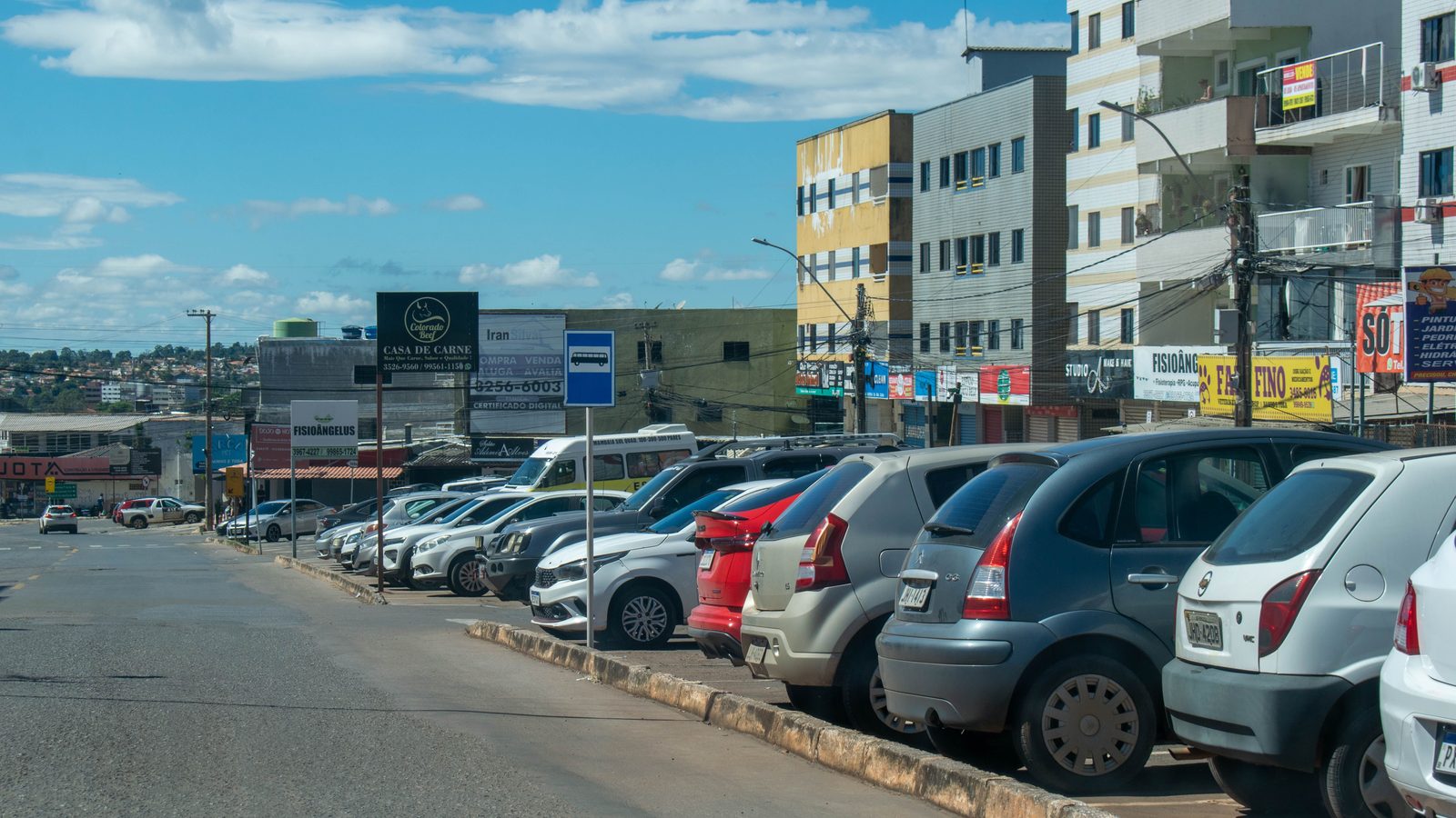 Rua comercial no Distrito Federal com carros estacionados ao longo da via.