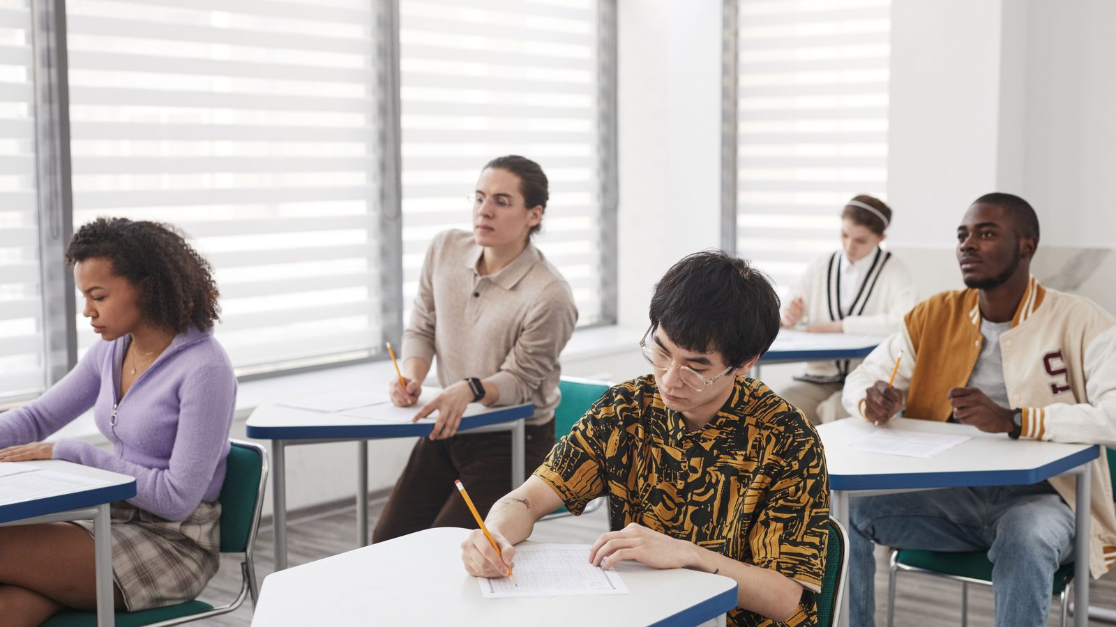 Estudantes fazendo prova em carteiras de uma sala de aula iluminada.