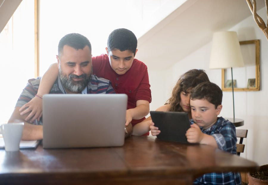 Pai e filhos pesquisando juntos no notebook, à mesa de casa.