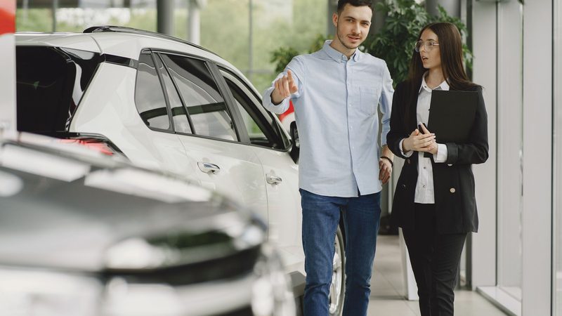 Cliente e vendedor conversando ao lado de um carro dentro de uma concessionária.