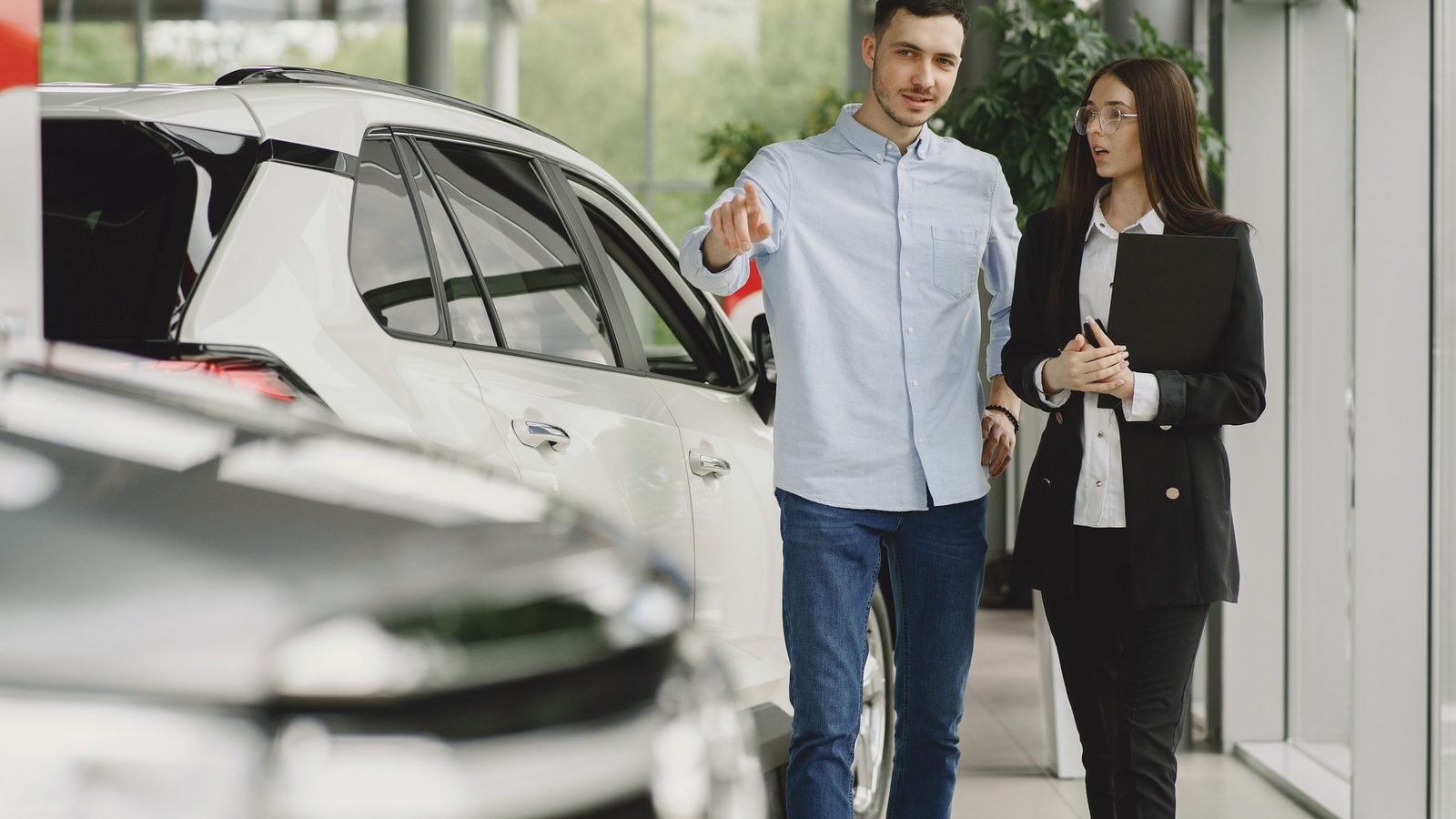 Cliente e vendedor conversando ao lado de um carro dentro de uma concessionária.