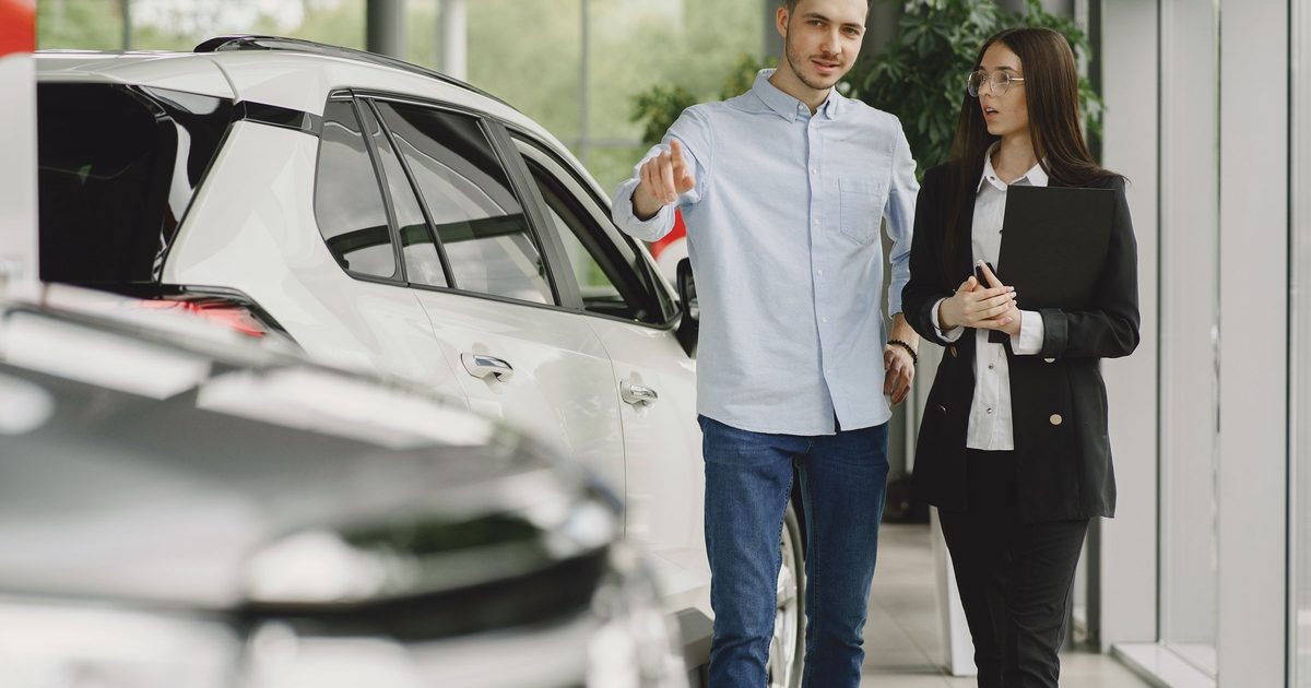 Cliente e vendedor conversando ao lado de um carro dentro de uma concessionária.