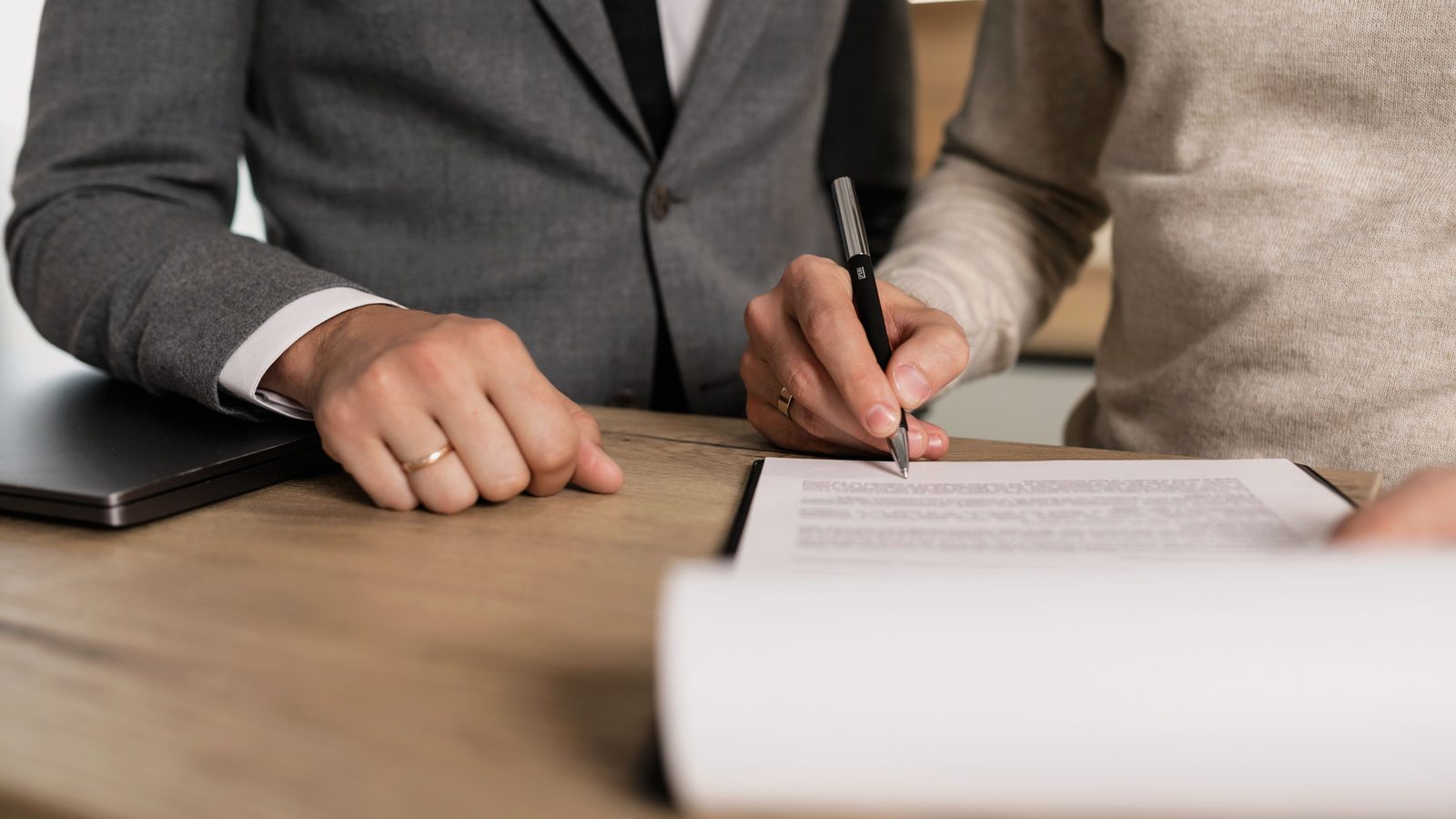Duas pessoas assinando documentos de contrato sobre uma mesa de madeira em um escritório.