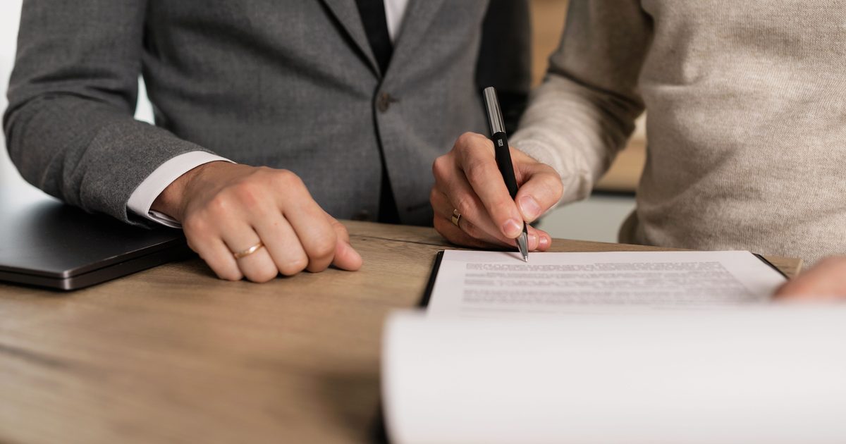 Duas pessoas assinando documentos de contrato sobre uma mesa de madeira em um escritório.
