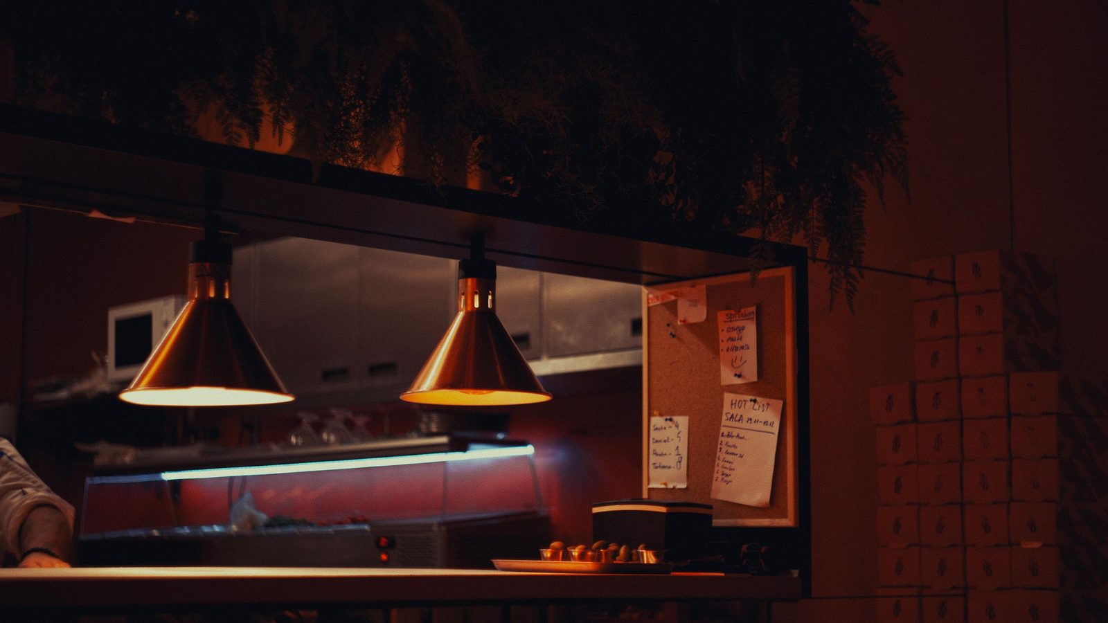 Cozinha de apartamento iluminada por luminárias no fim da noite, com bancada e armários acesos.