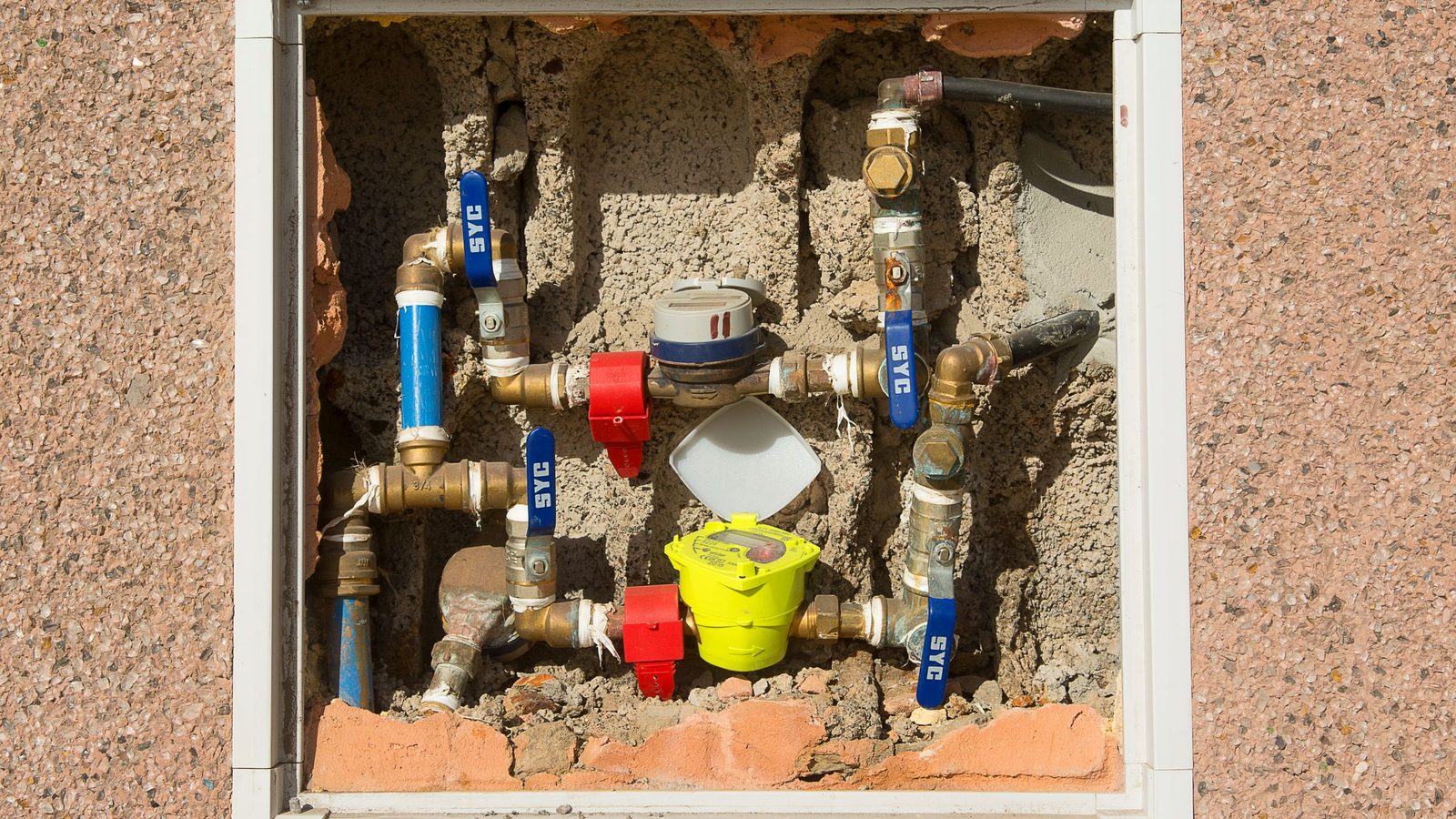 Hidrômetros instalados em um nicho de parede de concreto, com os registros aparentes.