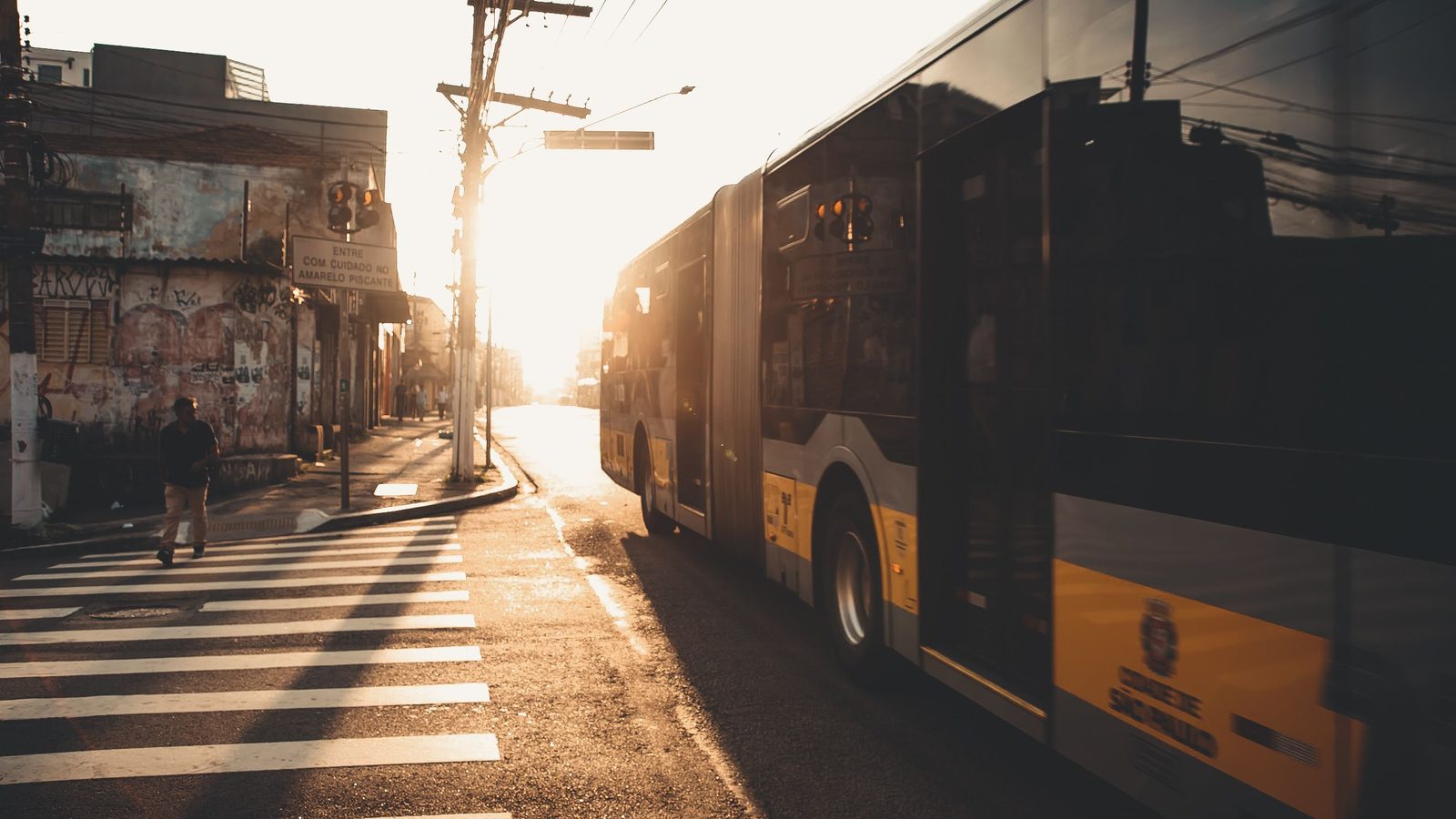 Ônibus urbano circulando por uma avenida no fim da tarde, com sombras longas sobre o asfalto.